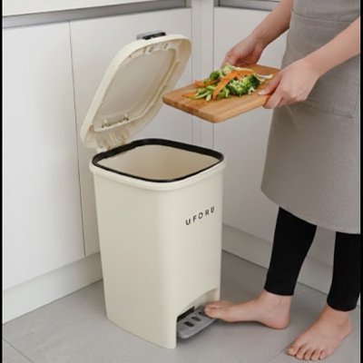 Personne tenant épluchures sur planche devant poubelle cuisine 